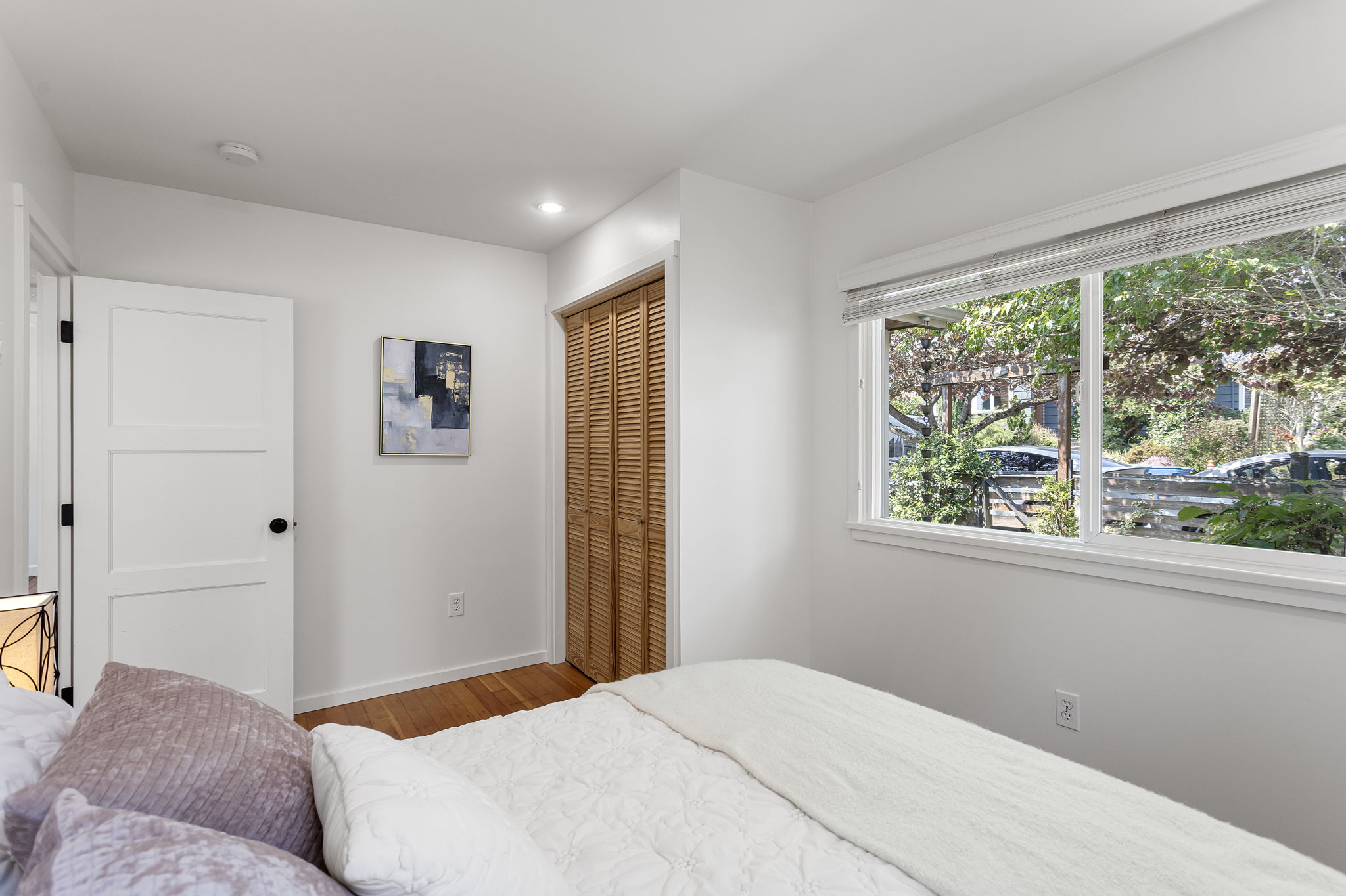 The wide front window looks into the garden canopy, giving the room a leafy outlook and some visual distance from the street.