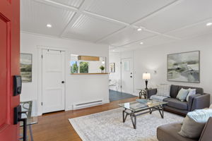 The red door opens straight into the living room—old-growth fir underfoot, paneled-and-beamed ceiling overhead, and a clear sightline toward kitchen and dining.