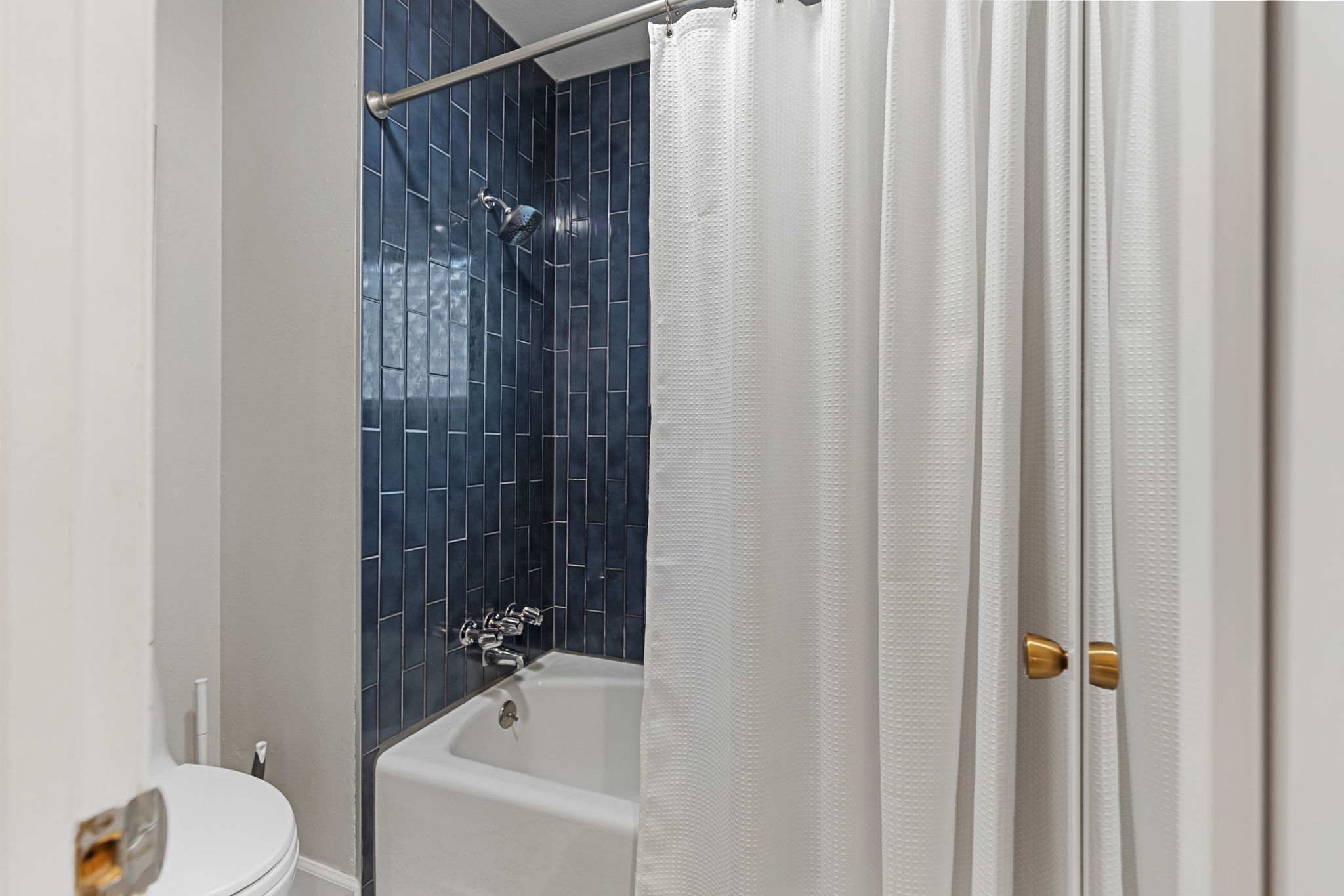 Full bath tub and shower combination accented by deep blue vertical tile work