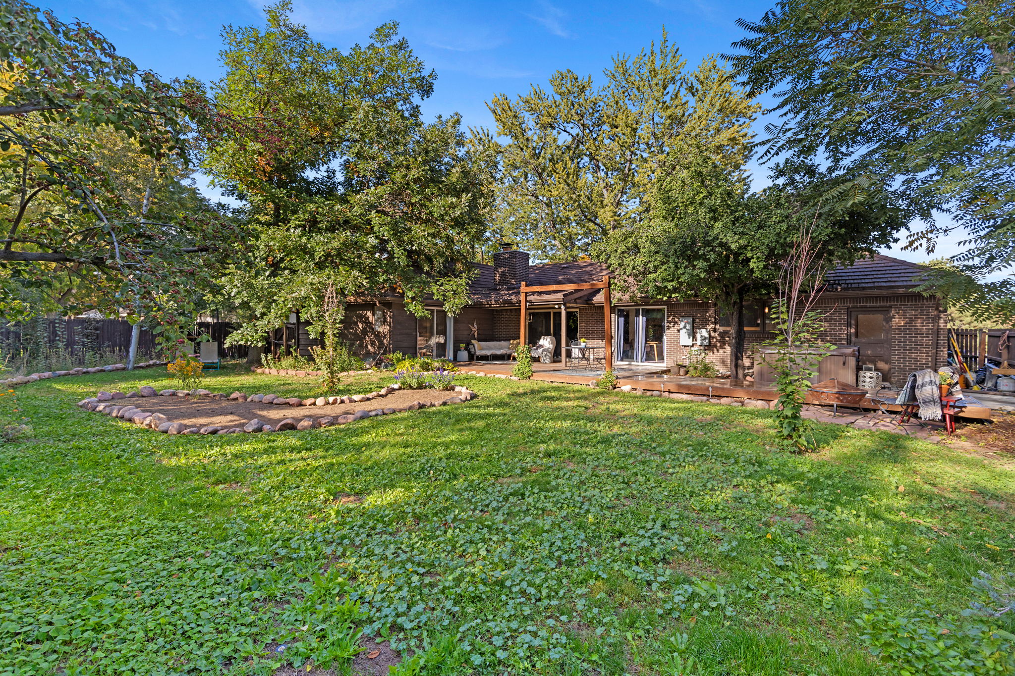 Expansive, fully fenced back yard with a large lawn, mature trees, garden beds, and multiple deck seating areas.