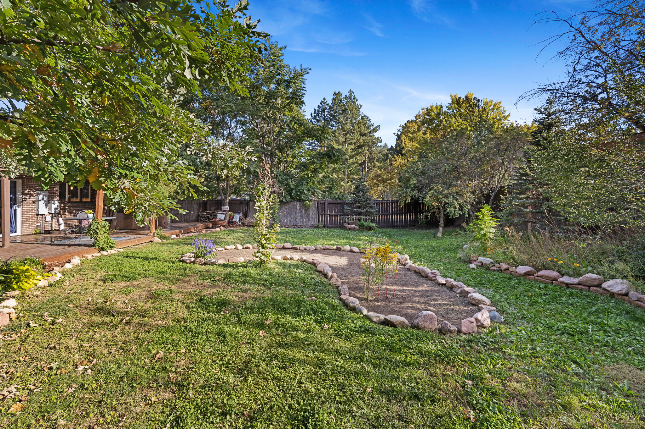Landscaped back yard featuring stone bordered garden beds, lush grass, and established trees