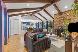 Open great room featuring vaulted, wood beam ceilings and a classic stone fireplace