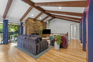 Vaulted ceiling with exposed wood beams, a stone fireplace, and new hard wood flooring throughout the main living space