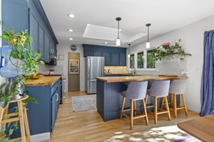 Updated kitchen featuring navy blue cabinetry, butcher block countertops, stainless steel appliances, and island seating