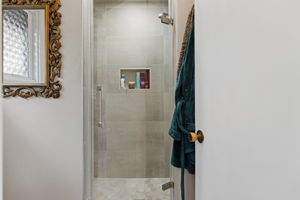 Upgraded walk-in shower featuring large format wall tile, built-in shelving niche, and glass doors