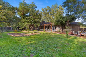 Expansive, fully fenced back yard with a large lawn, mature trees, garden beds, and multiple deck seating areas.