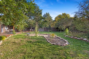 Landscaped back yard featuring stone bordered garden beds, lush grass, and established trees