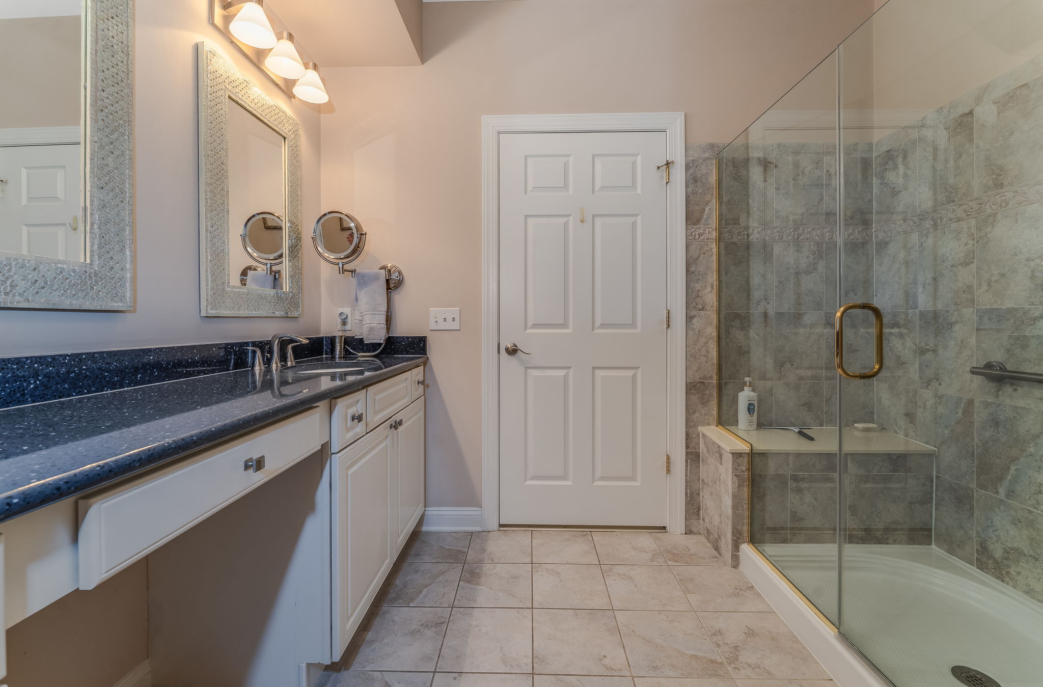 Master Bath The ensuite bath features double sinks and a make-up counter in a white vanity, and a shower in tile surround with bench seating and frameless glass door.