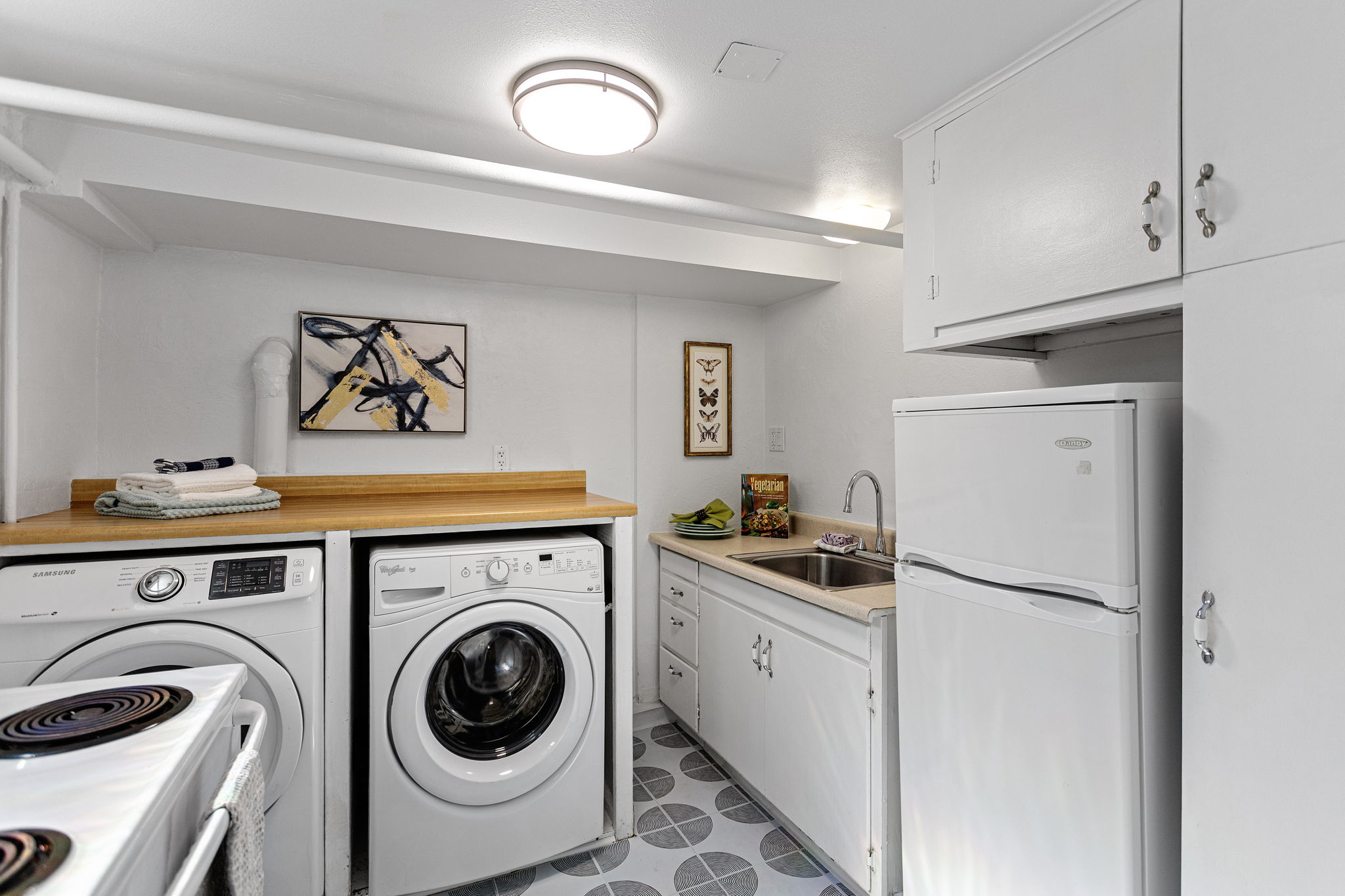 This shared kitchen/laundry serves both living zones, with refrigerator, range, sink, side-by-side washer/dryer and a window for daylight; its location also leaves room for a future owner to rethink how independently the two spaces function.