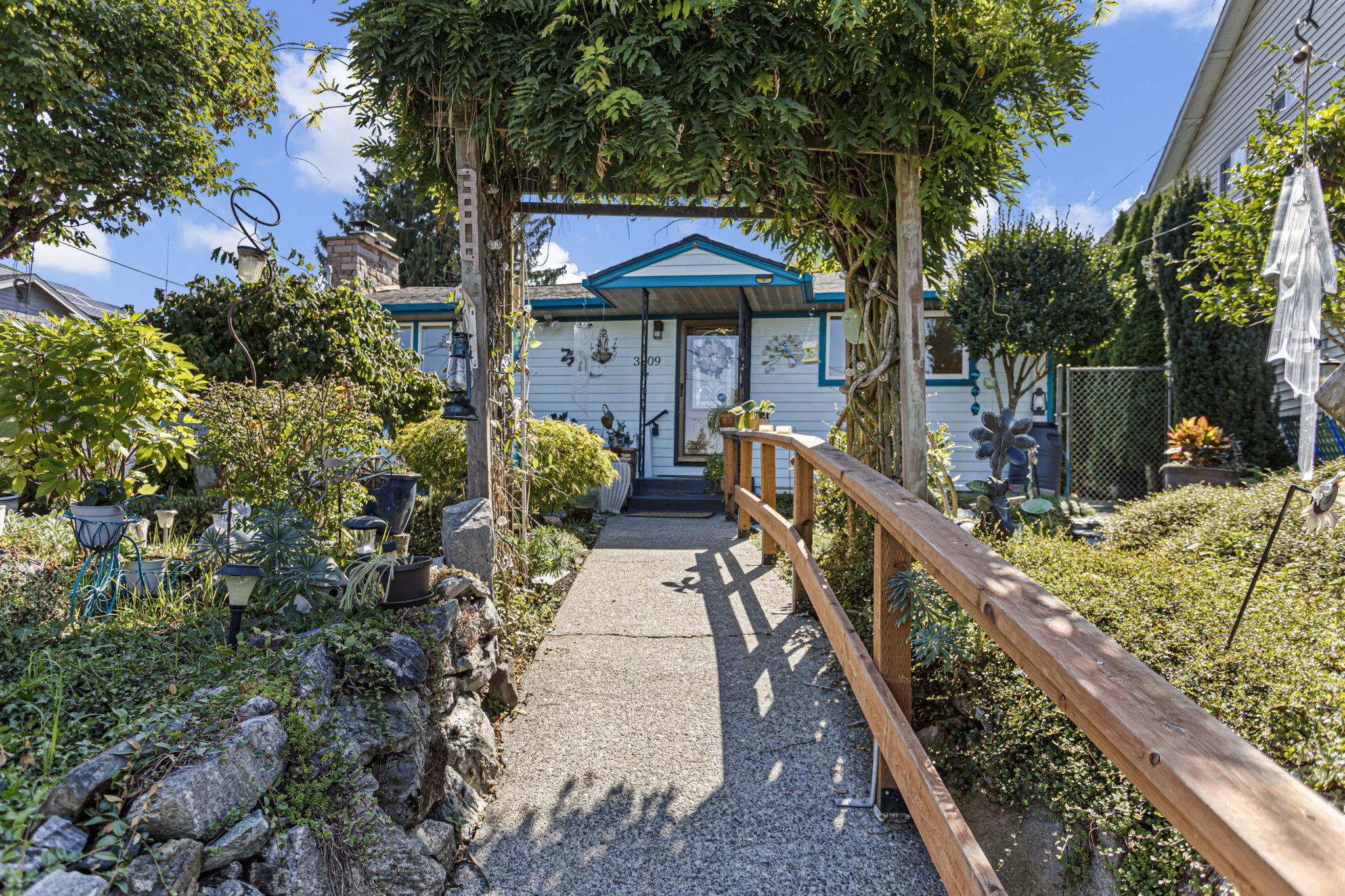 A vine-draped arbor frames the approach to the front door, with plantings unfolding on both sides.