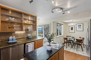 Under-cabinet lighting brightens the kitchen workspace, the rolling island adds flexible prep space, and the sightline carries through the dining area to the rear garden beyond.