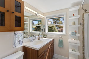 Garden views and late-day sun give the main-level full bath an especially pleasant outlook, with vanity storage and open shelving.