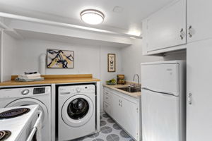 This shared kitchen/laundry serves both living zones, with refrigerator, range, sink, side-by-side washer/dryer and a window for daylight; its location also leaves room for a future owner to rethink how independently the two spaces function.
