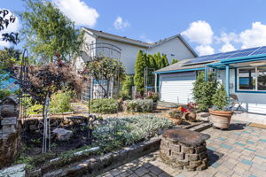 From the patio, established garden beds and trellises frame the rear of the home, with a built-in barbecue pit in the foreground and the owned 13-panel solar array overhead.