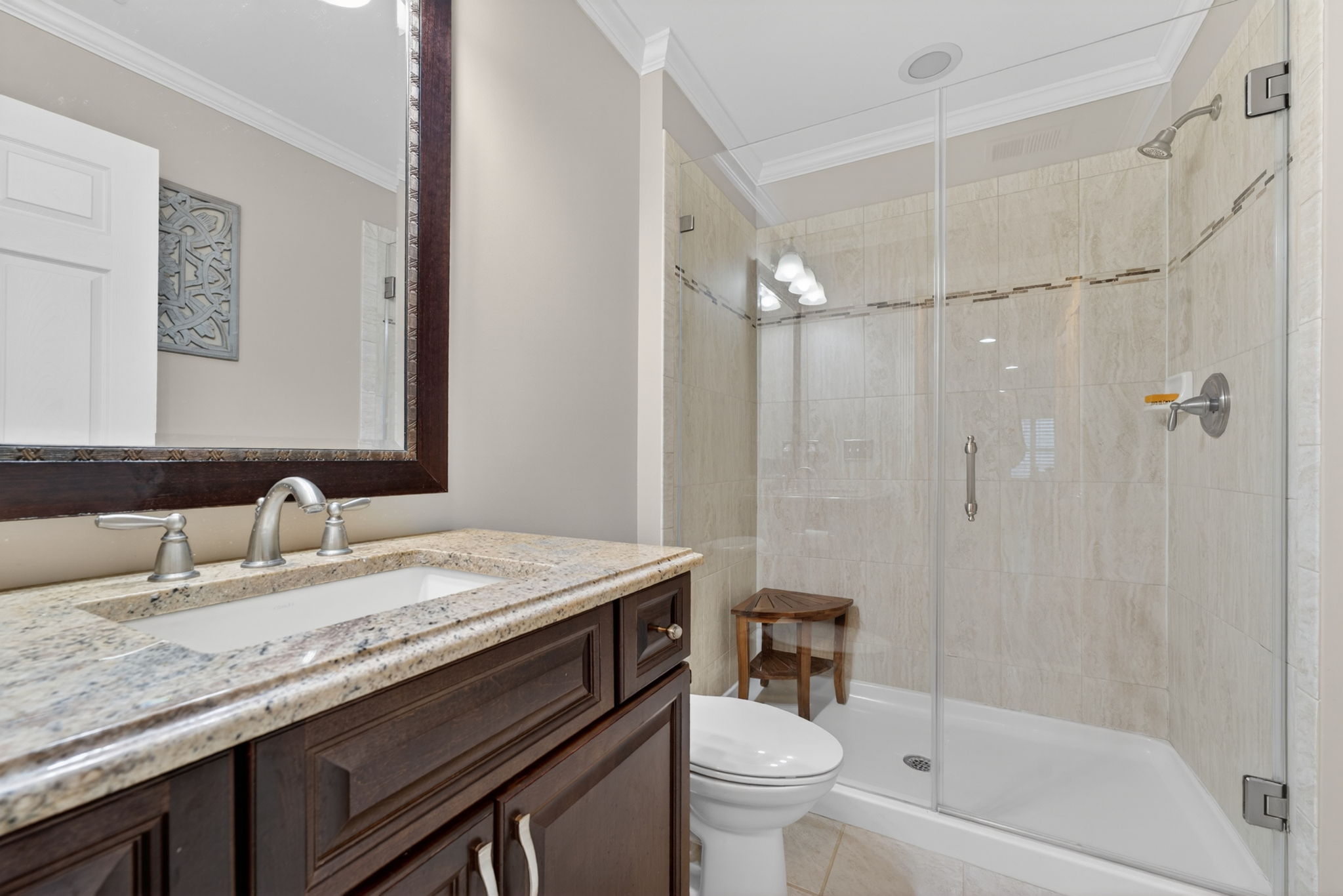 Full Bath Vanity with rectangular basin in a granite countertop, shower in tile surround with frameless door, ceramic tile flooring.