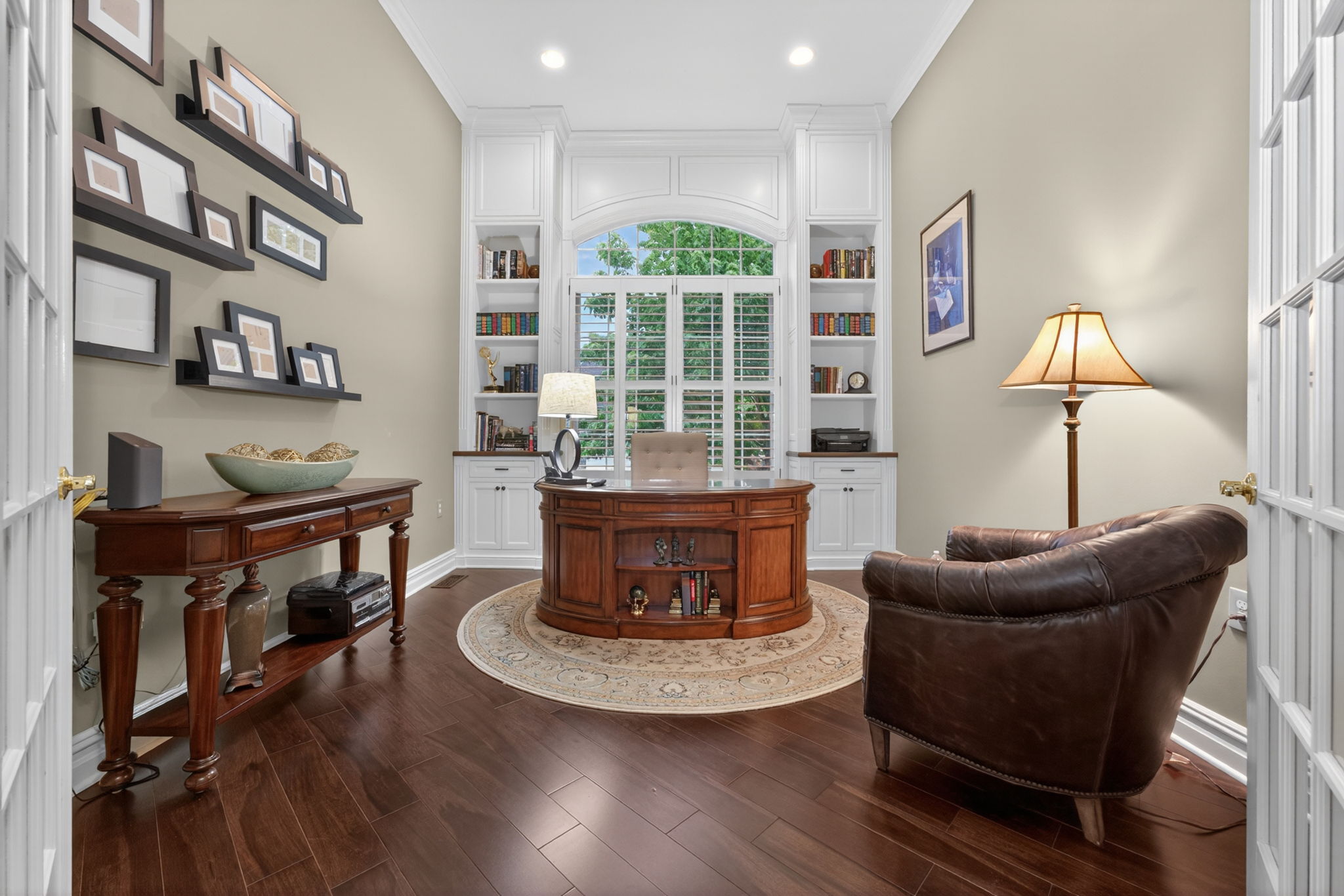 Study Double doors open to an impressive private study featuring a full wall of custom built-ins and a dramatic arched win-dow ̶ plantation shutters close for complete privacy.