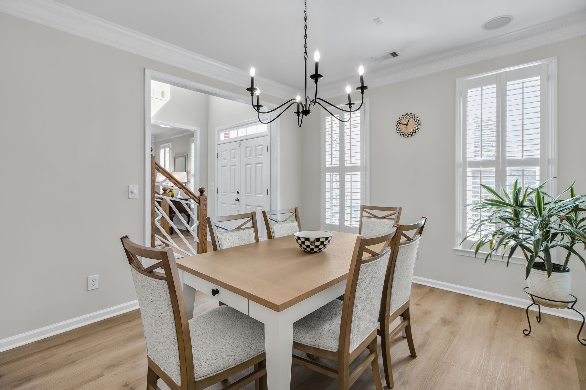 A formal dining room featuring a sleek black chandelier, LVP flooring, and large windows with plantation shutters, allowing for natural light to enhance the space.