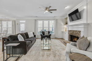 This bright and spacious family room features a beautiful stone fireplace, built-in shelving, and large windows that bring in natural light, creating a warm and inviting atmosphere for relaxation or entertaining.