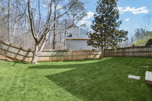 Fully fenced backyard with a lush lawn and mature trees, offering privacy and a safe play area.