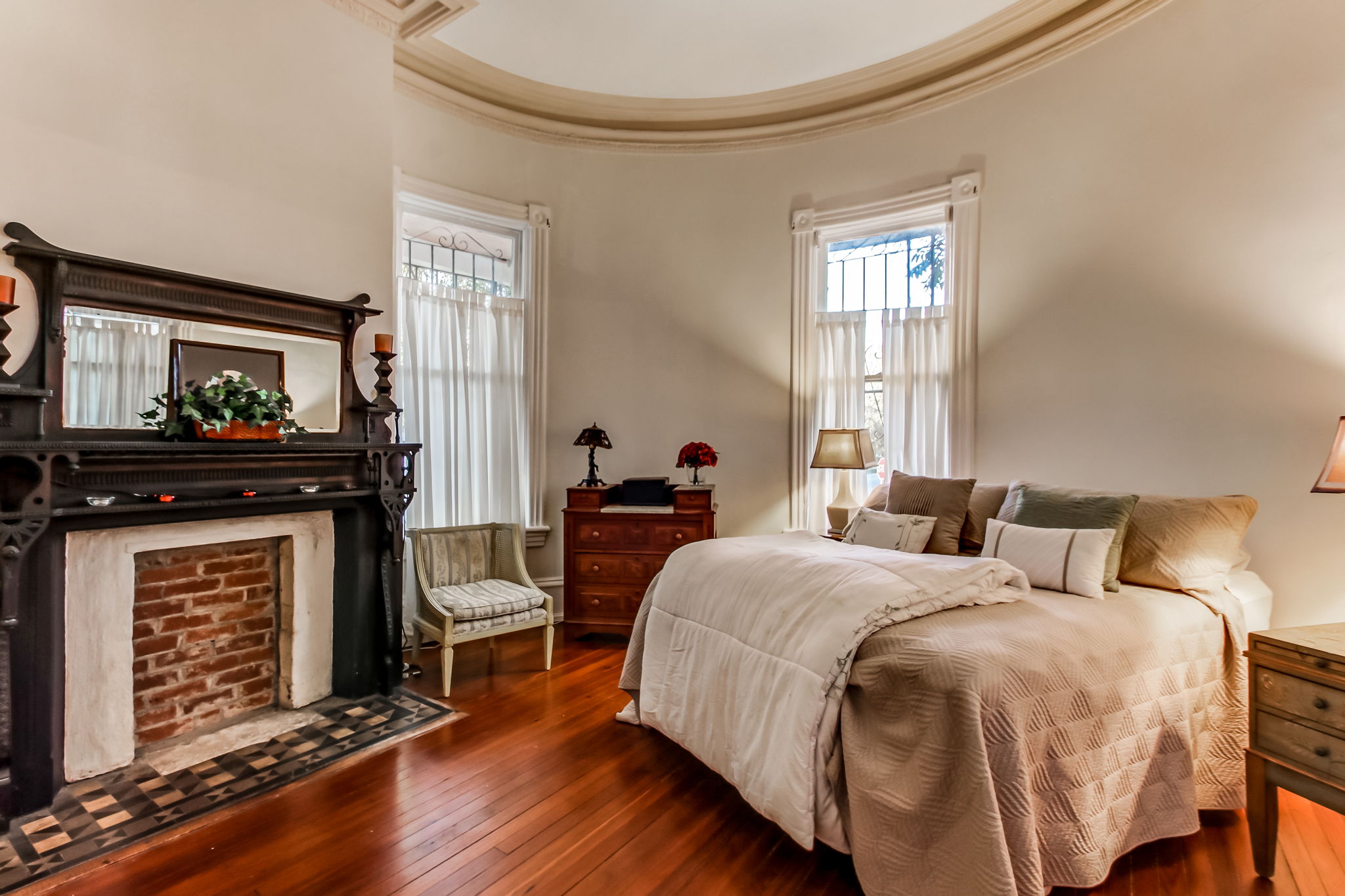 Main House Spacious Owner's Suite with with crown molding on ceiling, decorative mantel on fireplace, sitting area, and original hardwood floors.