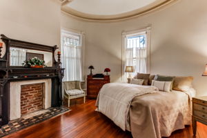 Main House Spacious Owner's Suite with with crown molding on ceiling, decorative mantel on fireplace, sitting area, and original hardwood floors.