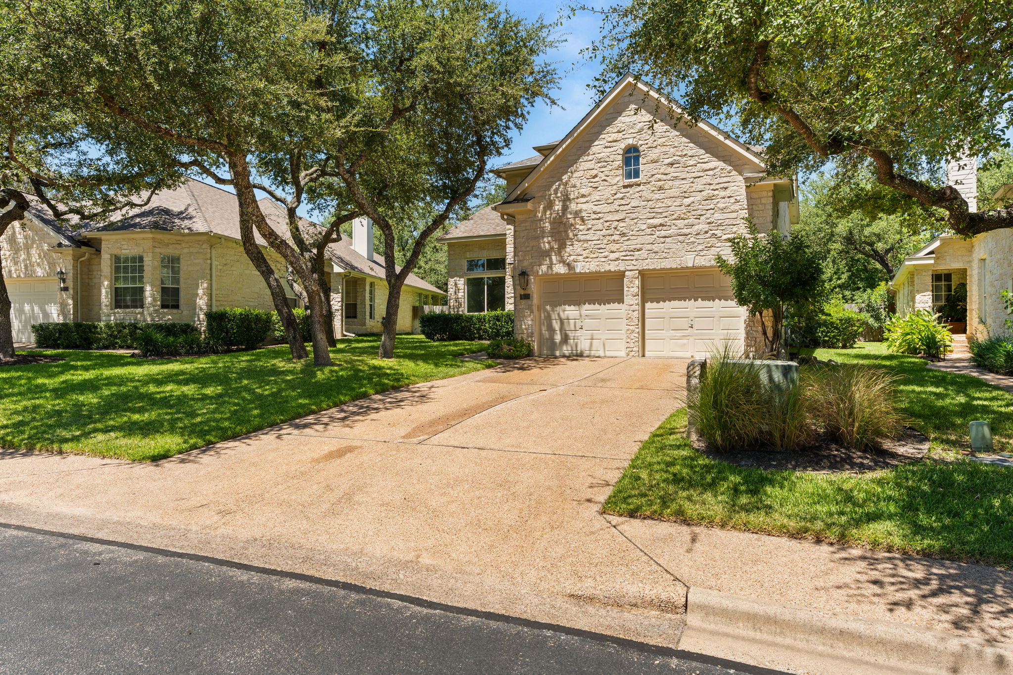 Tree-covered lot in prestigious golf course community. Large driveway leading to the 2-car attached garage. Front sidewalk.