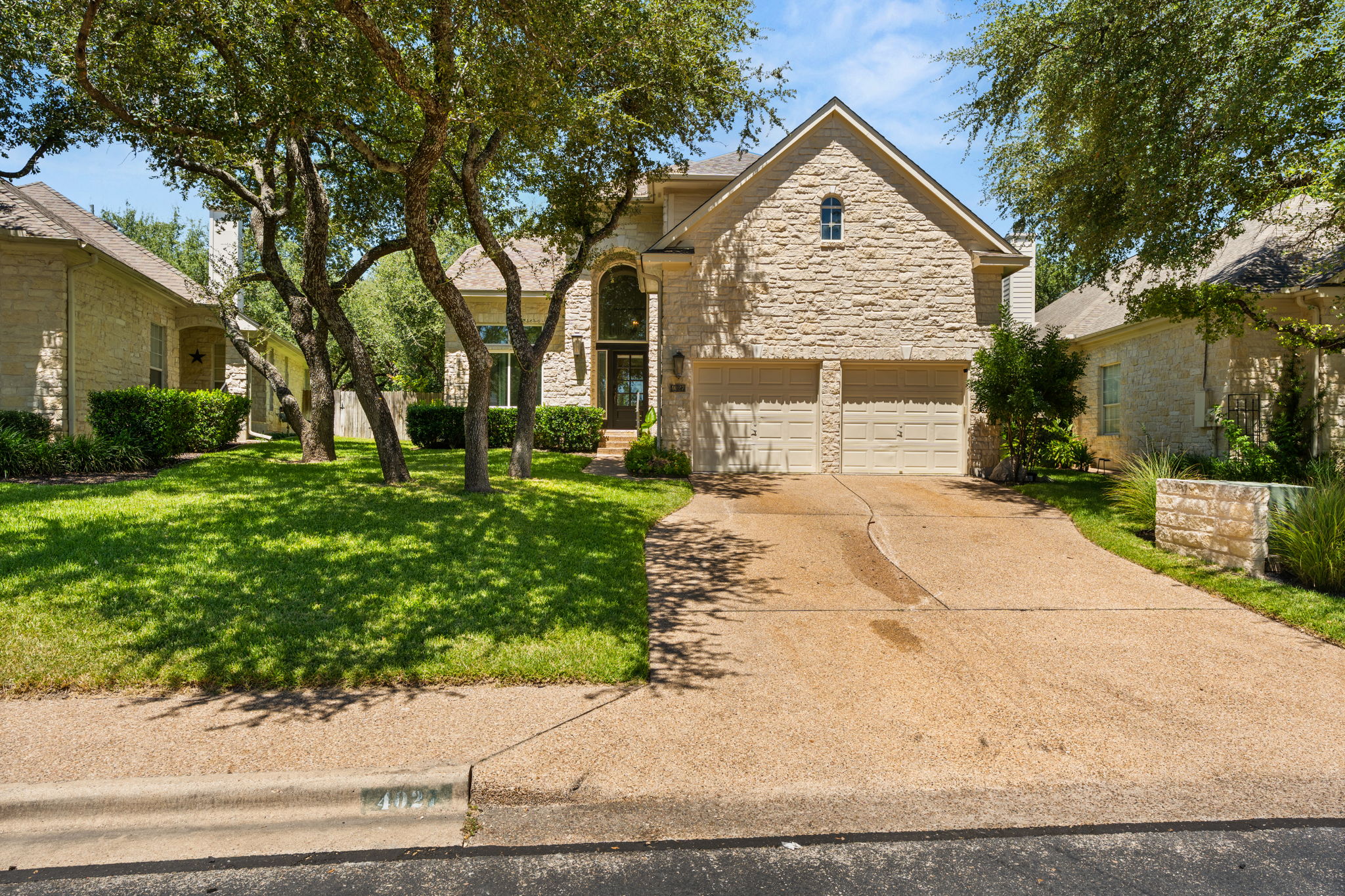 Tree-covered lot in prestigious golf course community. Large driveway leading to the 2-car attached garage. Front sidewalk.