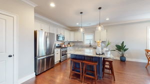 Large open white kitchen, with large island painted in accent color, granite countertops, and stainless steel appliances.