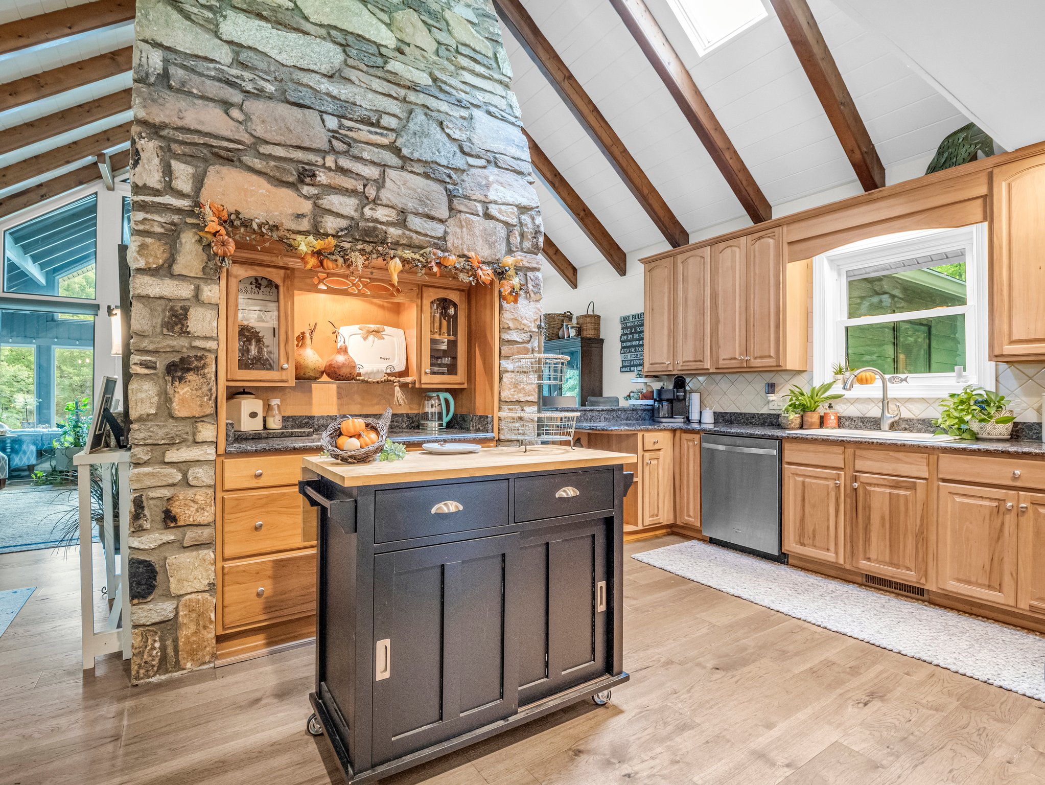 Gorgeous stone fireplace gracefully separates the kitchen and main living room, featuring a built-in niche with counter space, cabinets, and decorative and functional shelving.