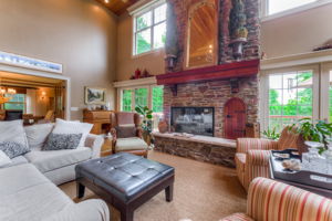 2 story living room with beautiful stone fireplace and large windows, leading out to spacious deck