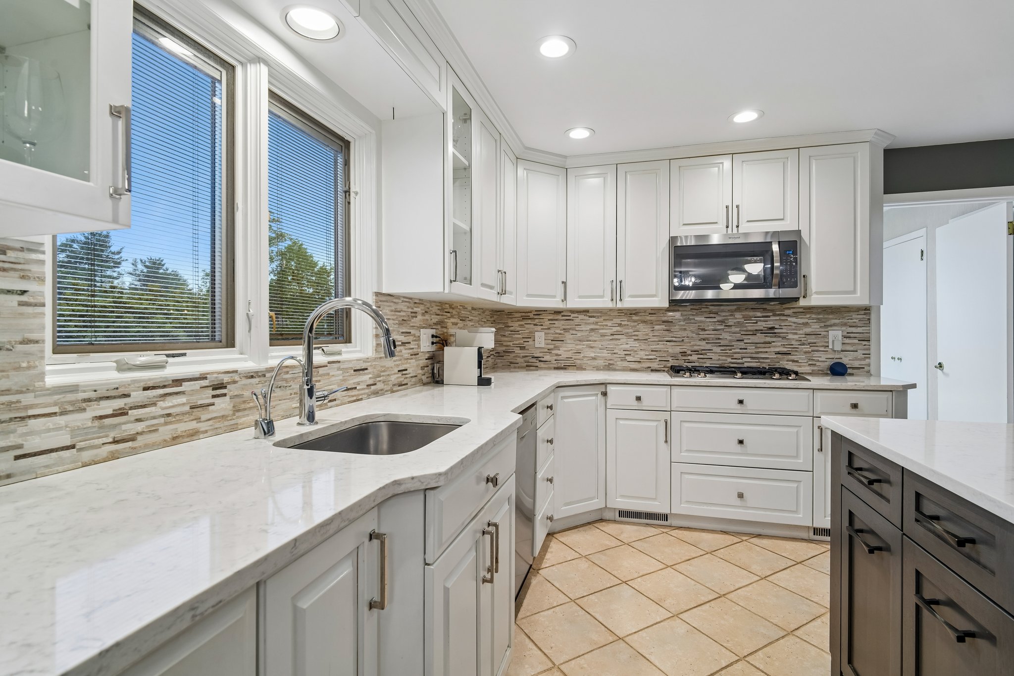 Natural light pours through the double windows above the sink, seamlessly linking gourmet kitchen to outside. Expansive cabinetry wraps the space, providing endless storage in a modern chef's kitchen.