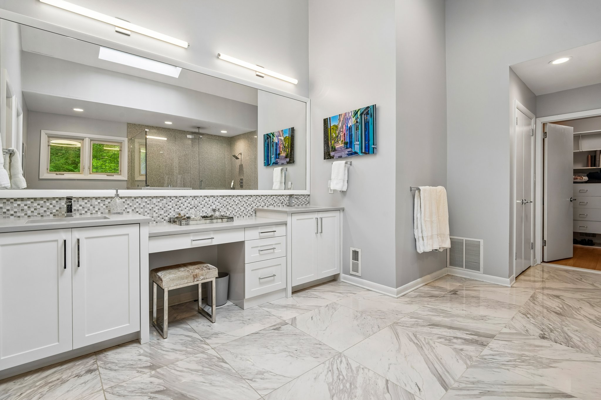 View of the dual sinks and dedicated make-up vanity with oversized wall mirror. In the back of the picture you can see the door to one of the two walk-in closets.