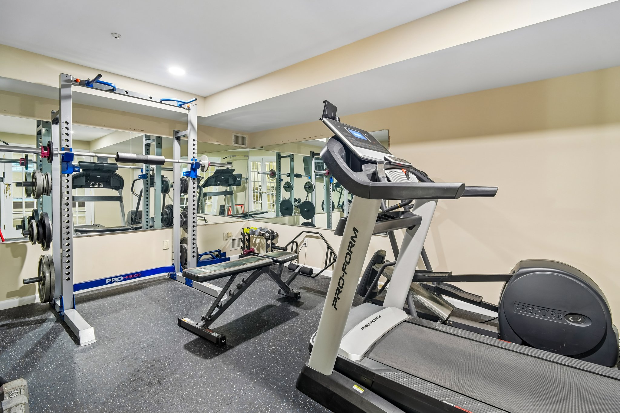 Dedicated lower-level home gym featuring professional gym flooring and mirrored walls. A spacious and bright environment designed to accommodate a variety of equipment and workout styles.