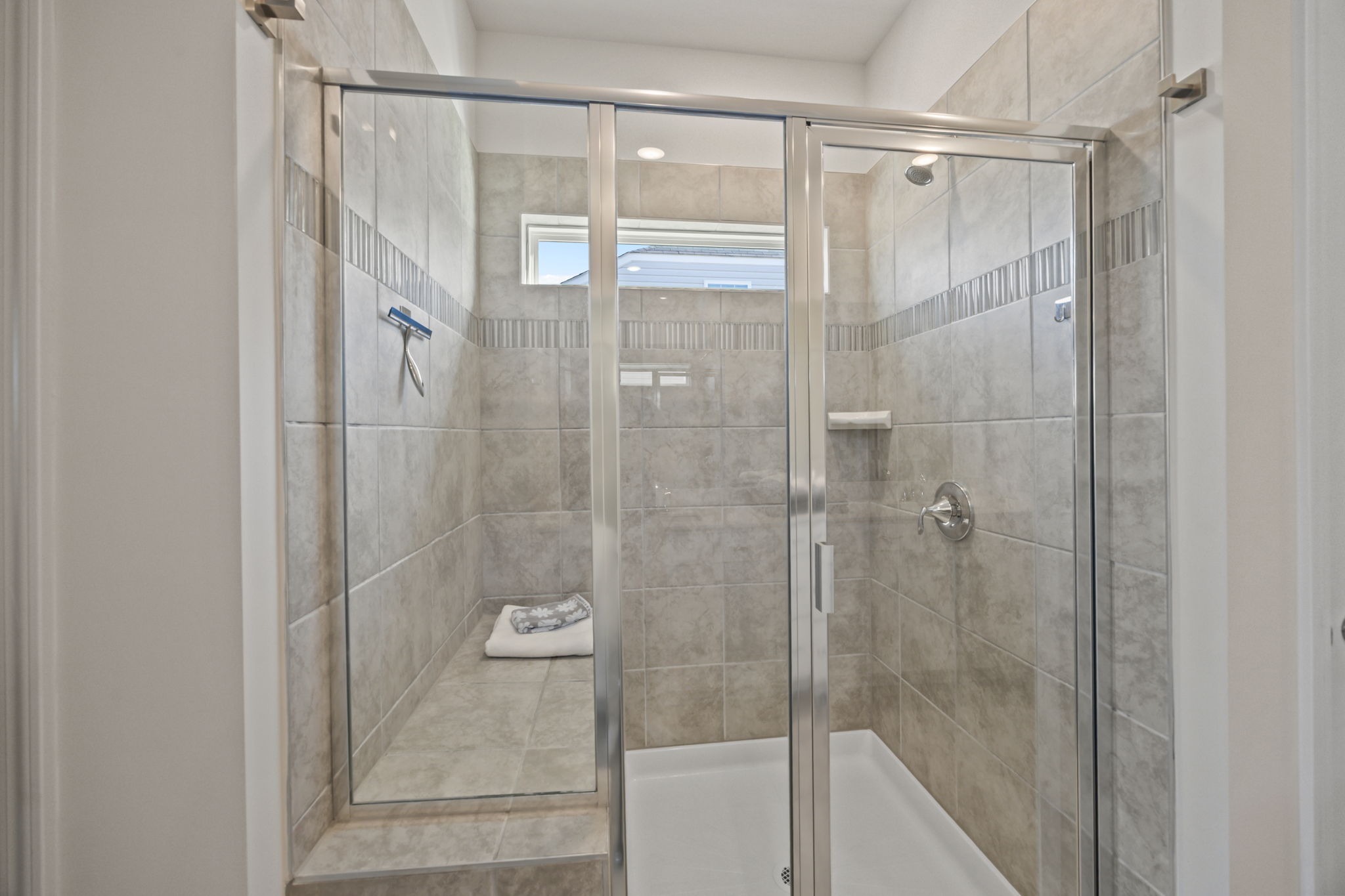 Shower in luxury! Large tiled shower with glass tile listel, clerestory window for natural light and seating.  Custom stainless towel/robe hooks already installed.