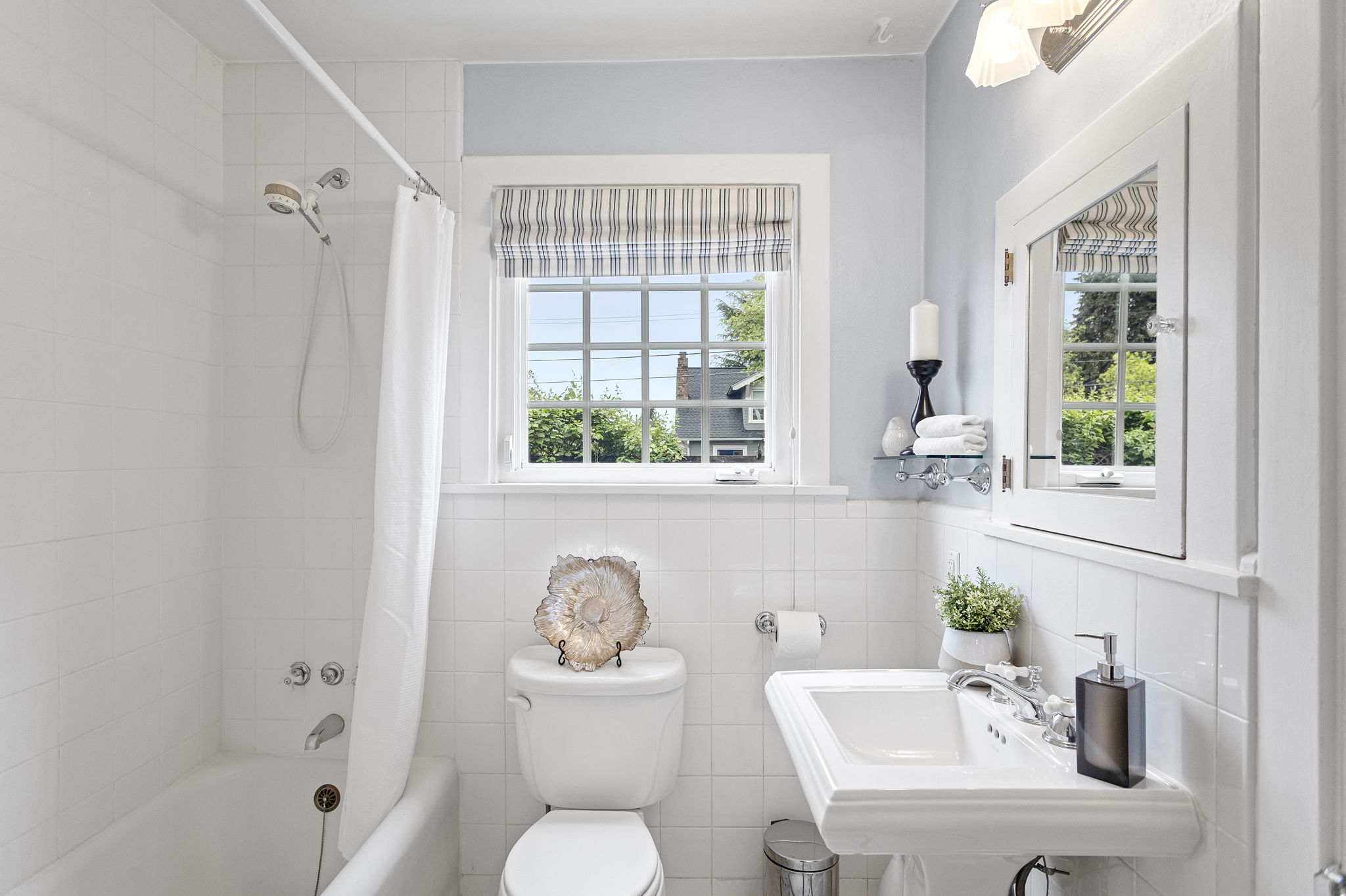 Pedestal sink, chrome cross-handle faucet, white subway tile wainscot, black and white mosaic tile floor with diamond border. The main floor bath didn't try to update itself — and it was right.