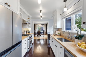 Looking back toward the dining room — the kitchen stays connected to the party. Marmoleum underfoot, cased opening straight ahead.