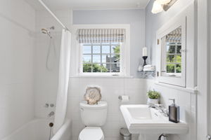 Pedestal sink, chrome cross-handle faucet, white subway tile wainscot, black and white mosaic tile floor with diamond border. The main floor bath didn't try to update itself — and it was right.