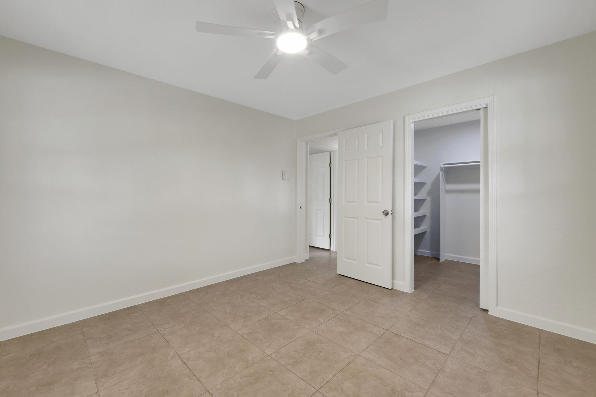 Primary bedroom additional features include a ceiling fan for comfort and two doors leading to a closet and an adjoining room, offering functional storage and connectivity.