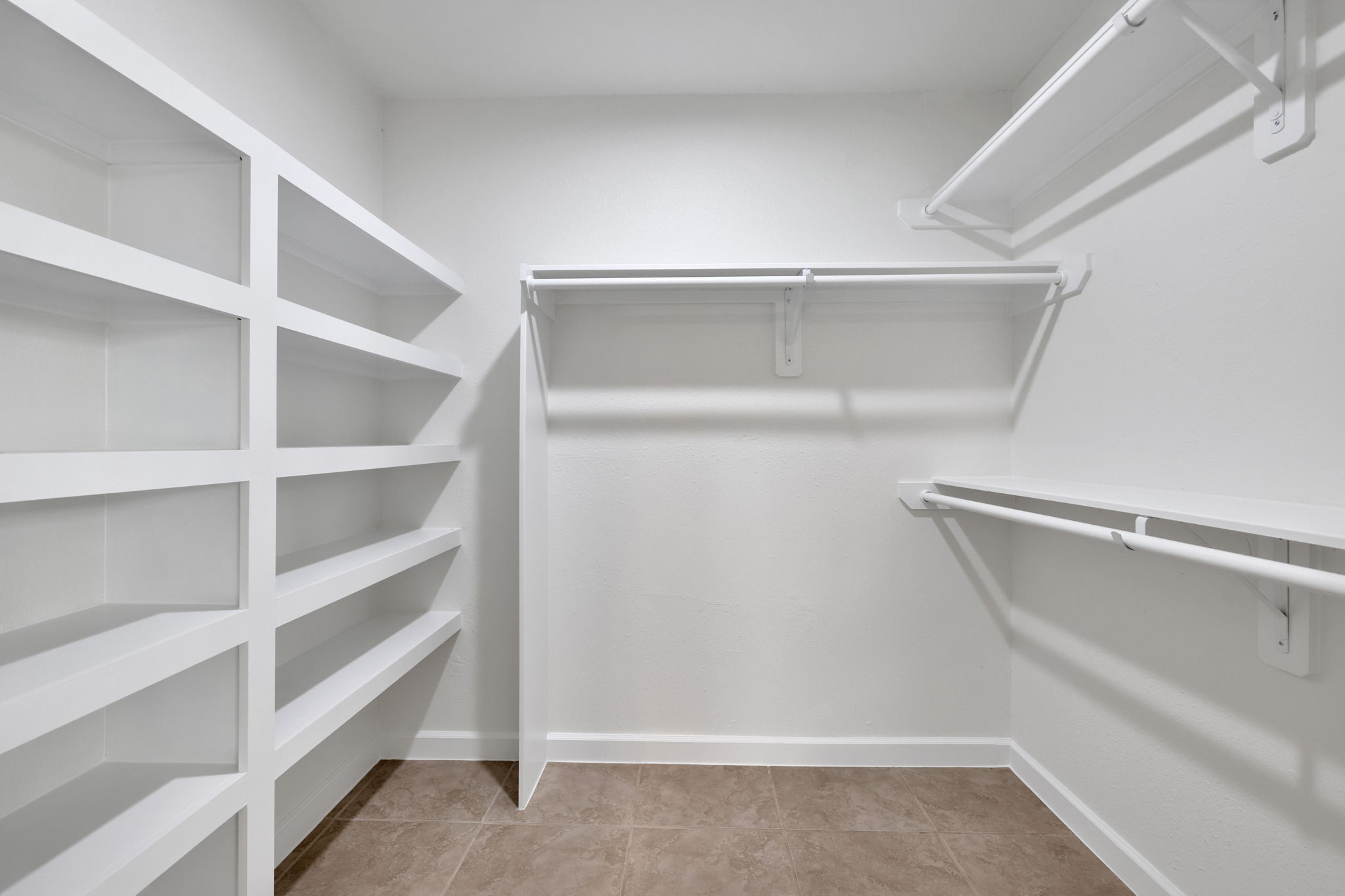 Spacious walk-in closet with multiple white shelves and clothing rods, perfect for organized storage.