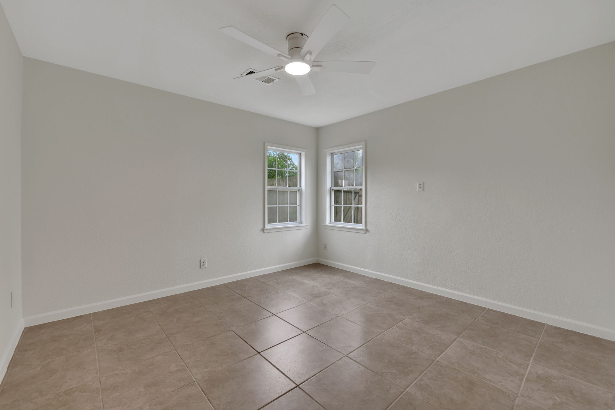 Secondary bedroom 2 features neutral walls, a ceiling fan, and large tile flooring, with two windows providing natural light. Ideal for a bedroom or office space.