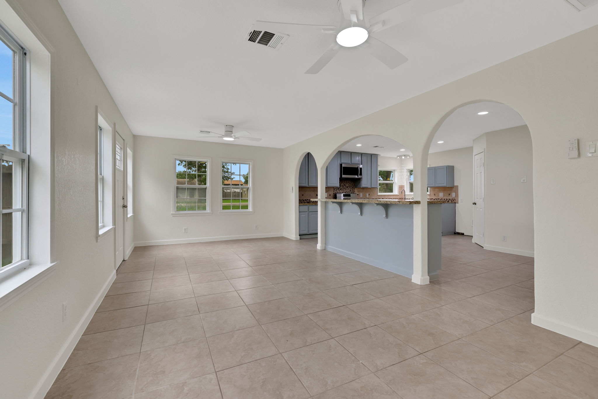 Bright and spacious open-concept living area with tile flooring, ceiling fans, and large windows. Features include arched entryways to a modern kitchen with updated appliances and ample natural light.