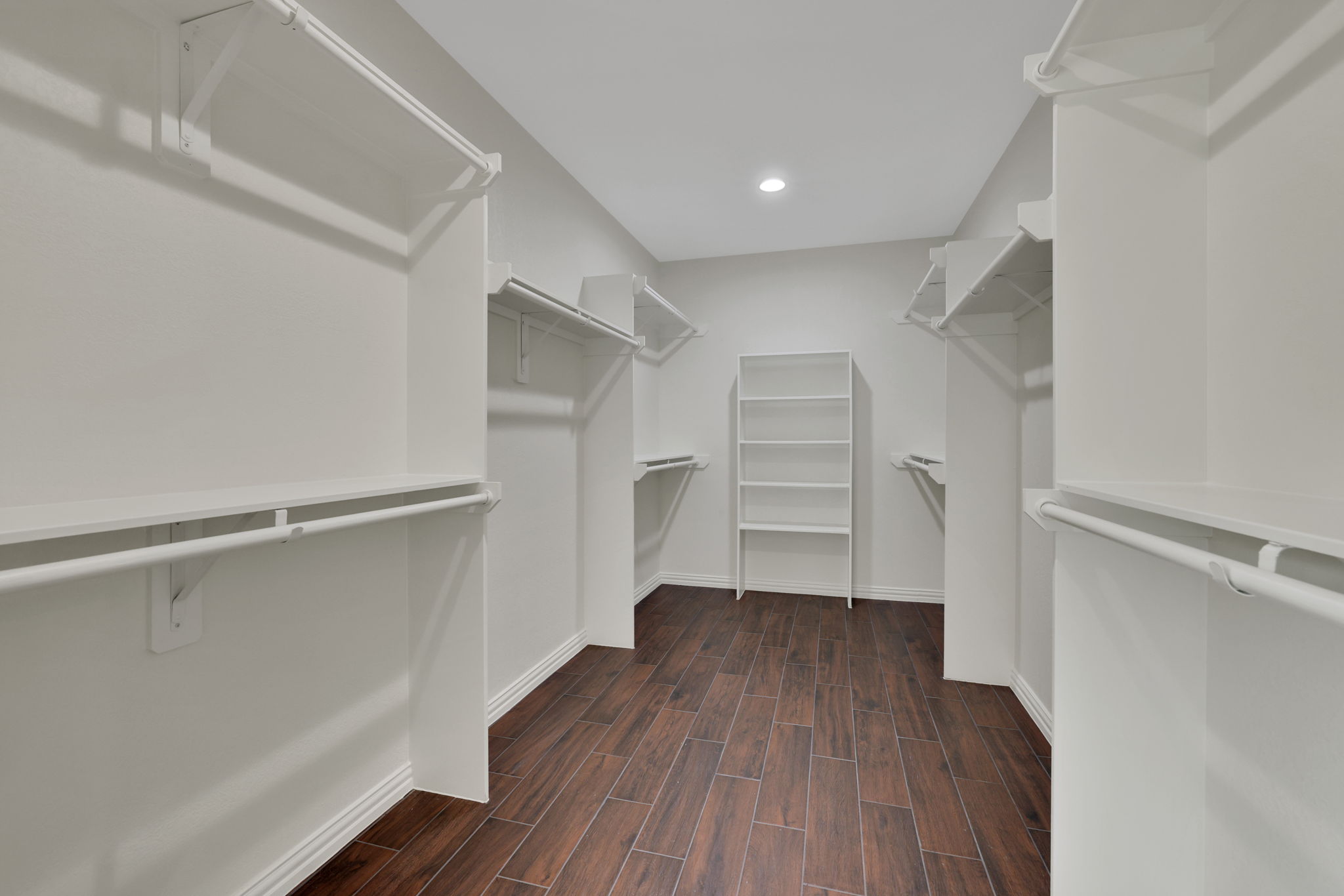Spacious walk-in closet with dark wood-look tile flooring, double-hanging clothing space, and built-in shelving for organized storage.