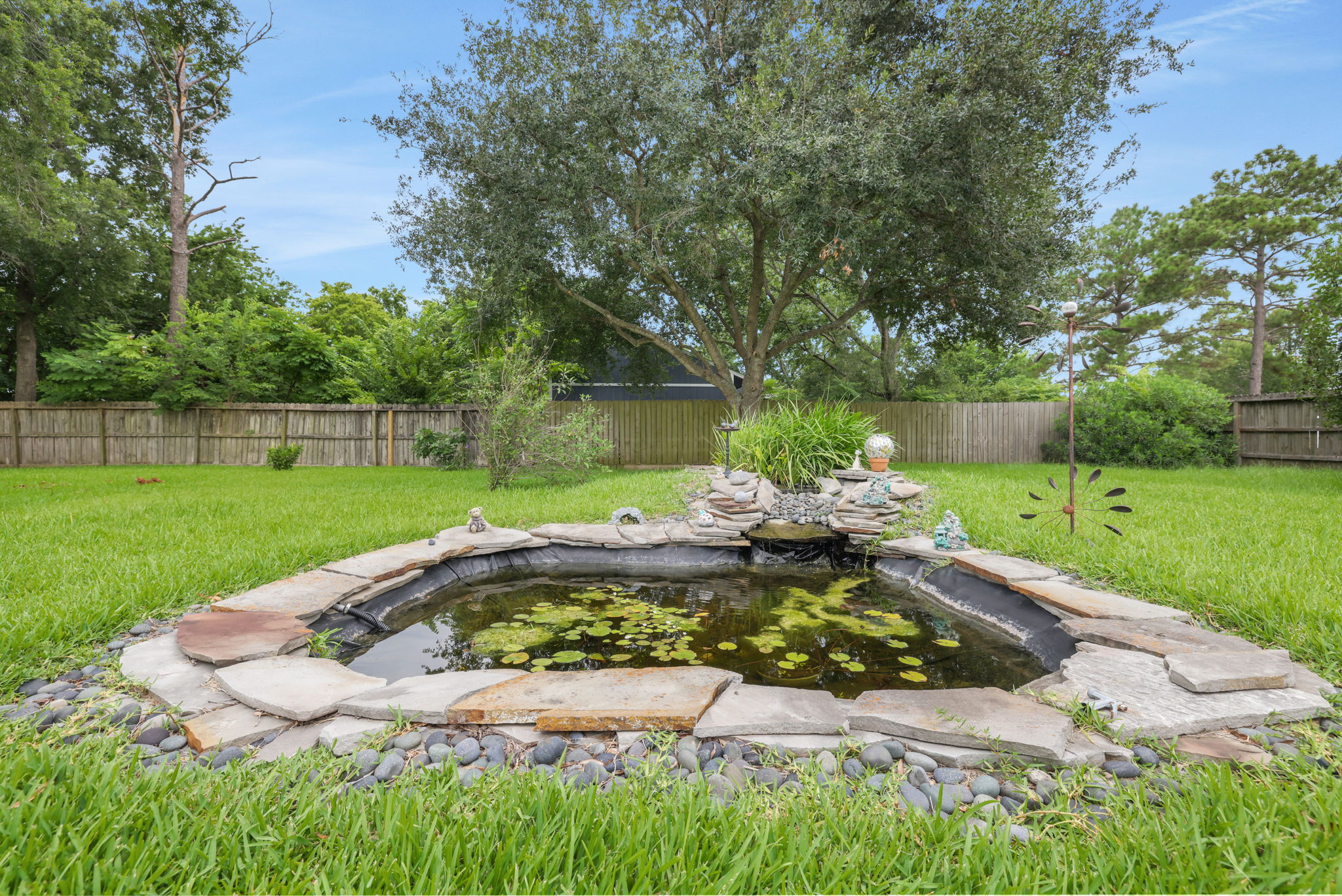 Serenity at its finest! This backyard features a pond with water lilies, surrounded by a stone border and lush greenery, creating a peaceful retreat.