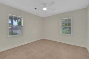 Primary bedroom features two windows providing natural light, neutral-toned walls, tiled flooring, and a ceiling fan, offering a bright and versatile space.