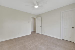 Secondary bedroom 1 with neutral-toned walls and tile flooring. It features a ceiling fan and two white doors, offering a clean and versatile space.