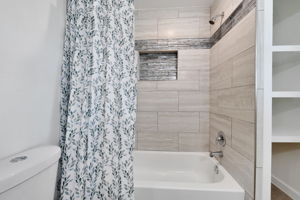 This bathroom features a tiled tub and shower combination with a decorative accent strip. It includes a built-in niche for storage.