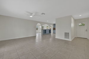Spacious open-concept living area with tile flooring, neutral tone walls, and circulating air. Arched doorways lead to a modern kitchen with custom cabinetry and ample natural light.