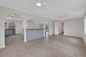 This spacious living area features tile flooring, neutral tone walls, and ample natural light. It connects seamlessly to the kitchen through elegant archways, offering an open feel.