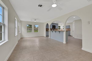 Bright and spacious open-concept living area with tile flooring, ceiling fans, and large windows. Features include arched entryways to a modern kitchen with updated appliances and ample natural light.