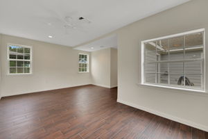 Spacious room with rich wood-look tile flooring, neutral tone walls, and ample natural light from three windows. Ideal for a living or dining area.